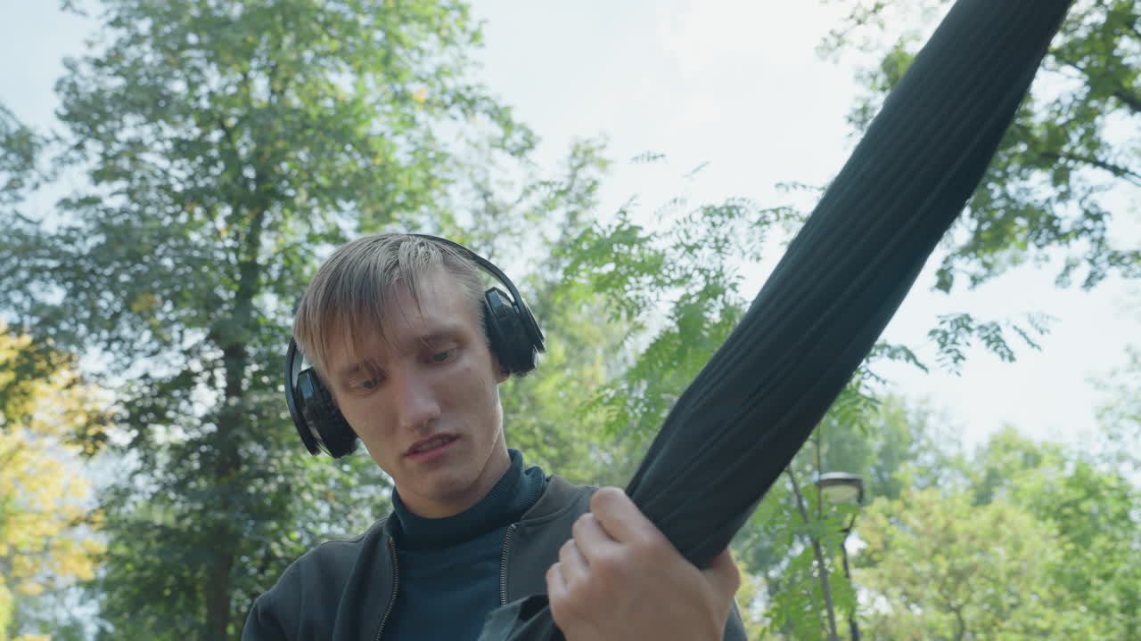 Un giovane che ripone un ombrello in un parco, goccioline che si formano sulla capote e primi piani con capelli bagnati che mostrano uno studente che piega l'ombrello, un pendolare che controlla il meccanismo, un ascoltatore che regola l'impugnatura e un primo piano delle stecche interne