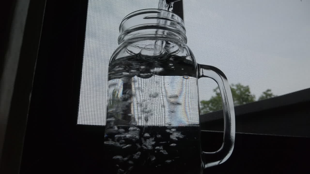 Water being poured into a tall glass jar, with bubbles percolating, close up