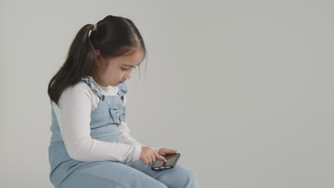 studio shot of young girl on asd spectrum gaming on mobile phone against white background 2