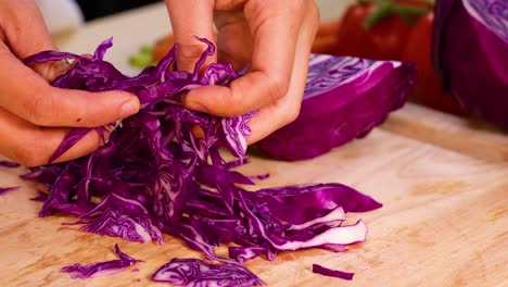 hands shredding red cabbage on a cutting board