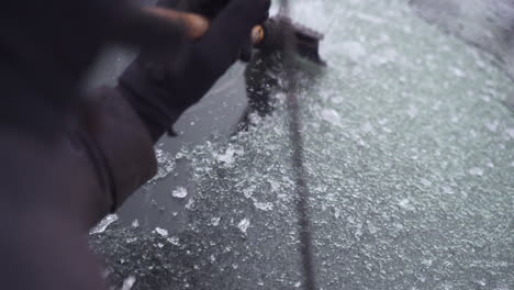 man cleaning and scraping ice from car windshield in snow