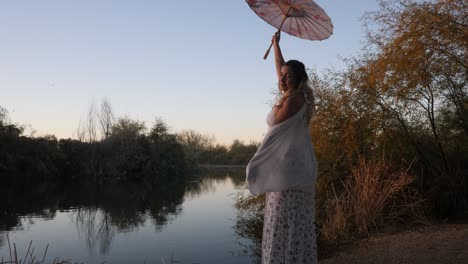 graceful woman spins umbrella during sunset next to a calm pond.