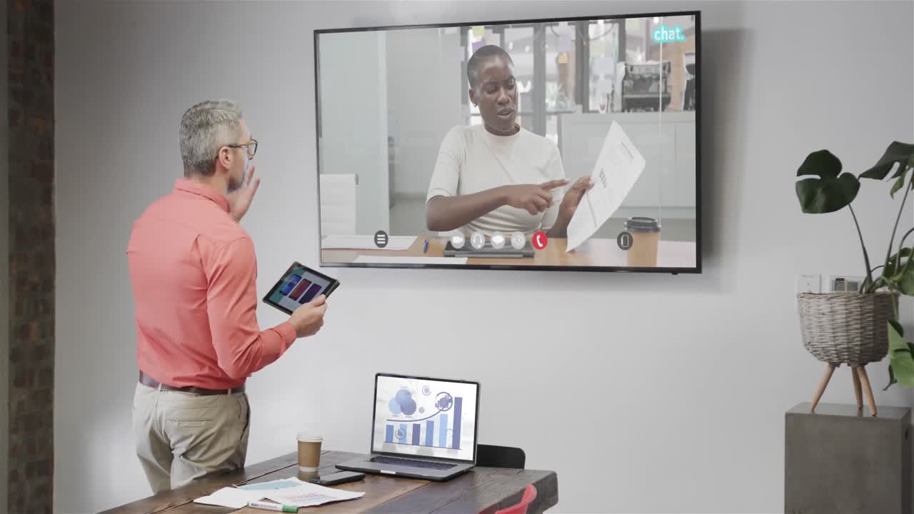 hombre de negocios caucásico en videollamada con una colega afroamericana en la pantalla de televisión