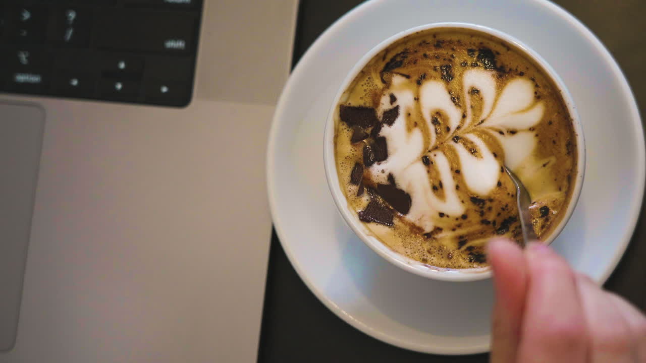 Slow motion shot of coffee art being stirred into the freshly made coffee at a computer