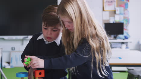 white girl and boy working together with toy construction blocks in a primary school class, close up