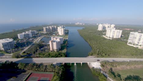 aerial 4k drone footage of along the vanderbilt channel and over cars driving along bluebill avenue bridge back and forward to wiggin pass beach in naples, florida, usa