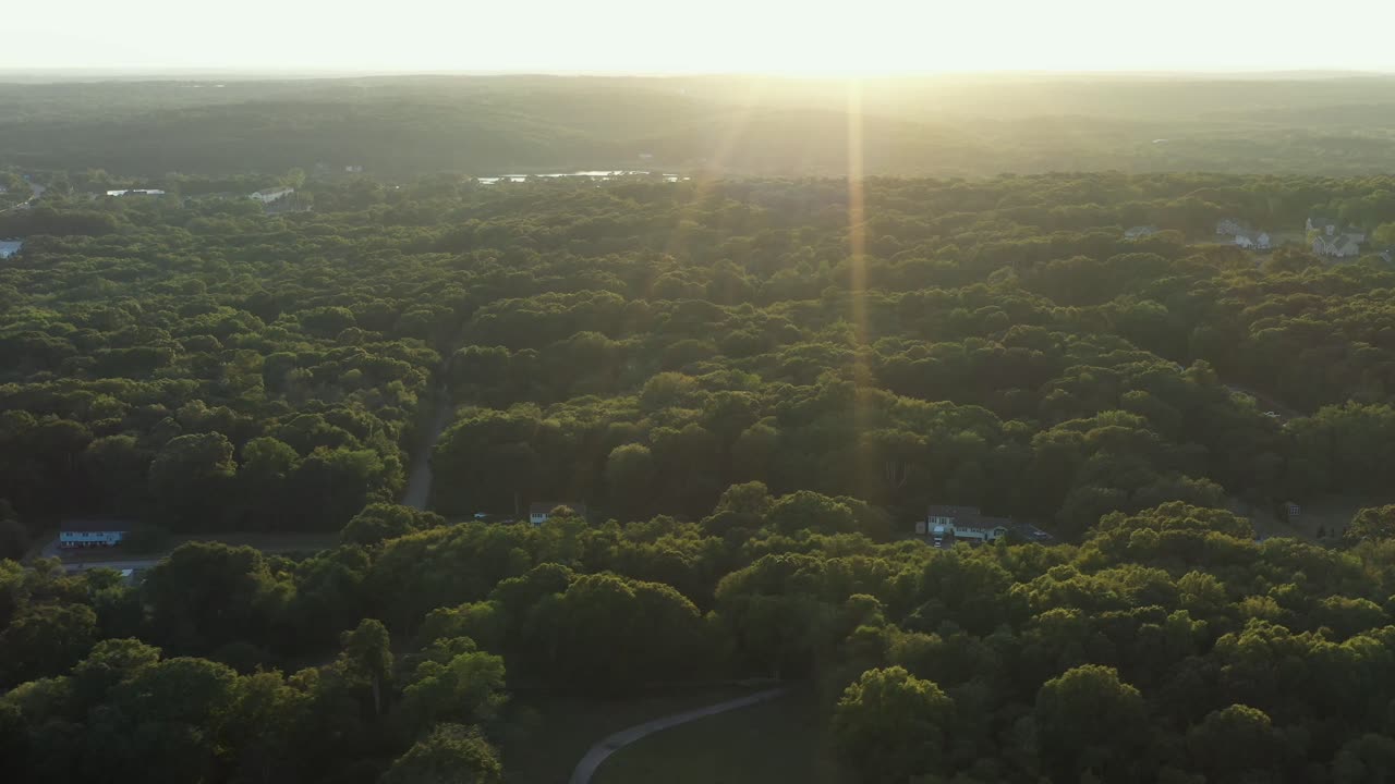 angled reverse flight over a rural area of the Northeastern USA in the forest with a bright sunset, with intense lens flare