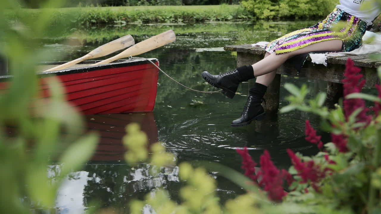 Woman relaxes by lake on wooden jetty dangling feet and touching water surface