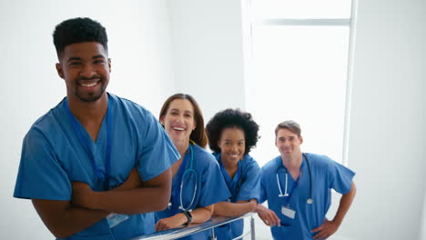 portrait of smiling multi cultural medical team wearing scrubs standing on stairs in hospital