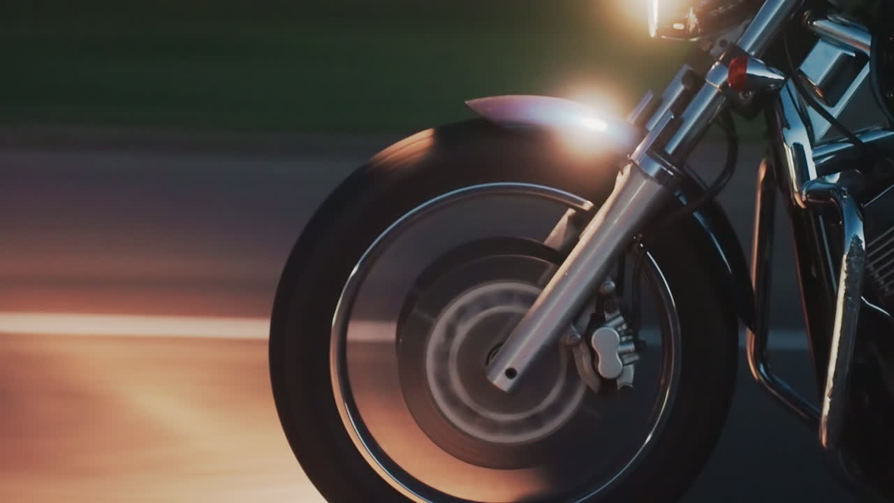 Close up of two bikers wearing helmets and leather jackets riding motorcycle in evening light, faces partially visible through visors, with background fading into dark forest scenery in motion