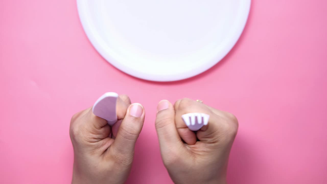 manos sosteniendo un cuchillo y un tenedor de plástico en una superficie rosa con una placa blanca