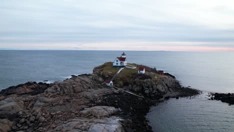 Short-Orbit-of-quaint-lighthouse-atop-a-rocky-island-with-dusky-sky-over-the-Atlantic-ocean