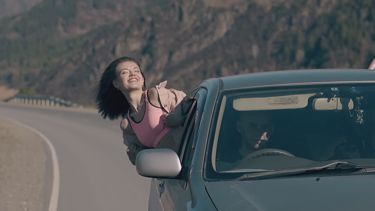 bruneta eufórica se inclina hacia fuera del coche ríe y disfruta de la vida