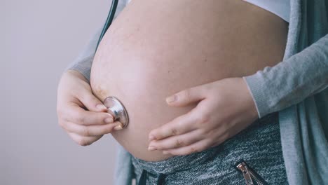 pregnant woman touches baby bump with stethoscope closeup