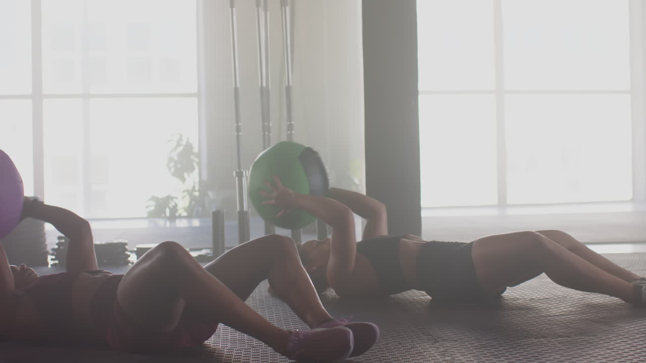 Exercising with medicine balls, women doing sit-ups in gym, focusing on fitness