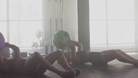 exercising with medicine balls, women doing sit-ups in gym, focusing on fitness