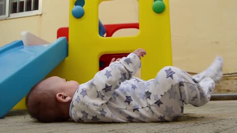 tree-months-old-baby-boy-streching-his-legs-on-the-carpet-in-backyard-while-plastic-play-house-is-in-the-background