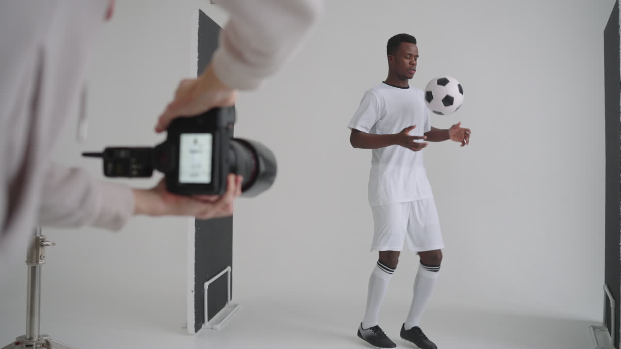 Behind-the-scenes photo shoot: A photographer in a photo studio uses a flash for photos of a black professional football player. Photo shoot in the studio of a sports magazine advertising