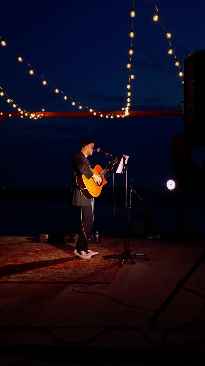 Mann som spiller akustisk gitar og synger på utendørsscene om natten