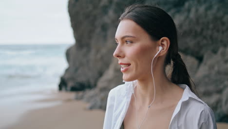 woman answering phone headphones standing beach in front sandy hill close up.