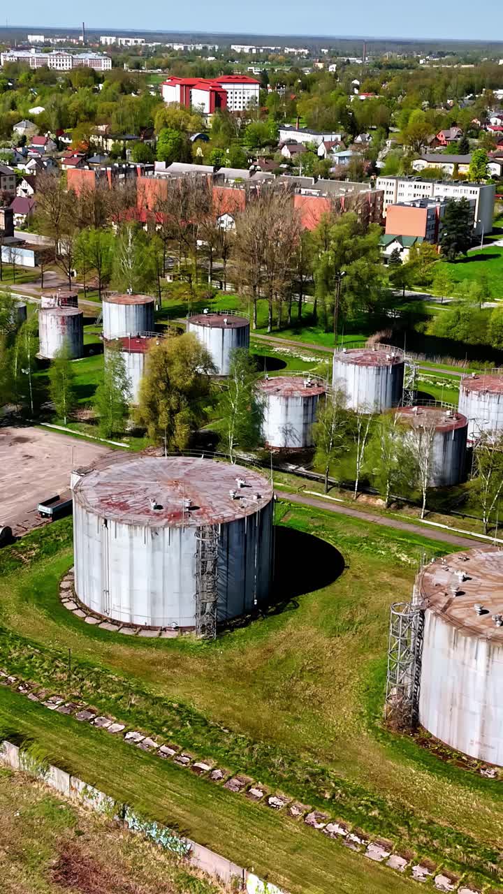 Aerial view of rusty industrial storage tanks near a green suburban area in Latvia