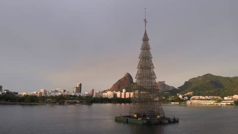 panning around the tallest floating christmas tree in the world in 2018 situated in the city lake of rio de janeiro with the city landmarks two brothers peak and gavea rock in the background