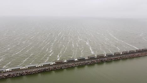 Wide-aerial-pan-of-long-freight-train-on-straight-track-by-sea-in-Argentina