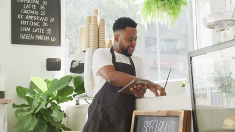 afrikanisch-amerikanischer cafe-besitzer mit laptop und tablet im café