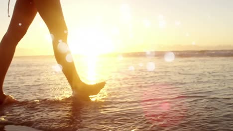 woman walking barefoot in ocean on the sand against sunshine on ocean