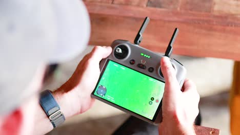 close-up of hands operating a drone controller with a green screen display in a well-lit outdoor setting
