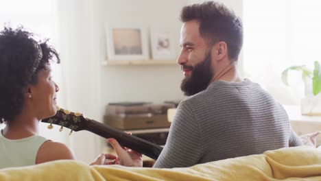 video de la vista trasera de una feliz pareja diversa en casa, el hombre tocando la guitarra, cantando a la mujer, copia el espacio