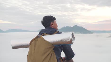 asian hiker male sitting on the mountain enjoys seeing beautiful view of top foggy mountain