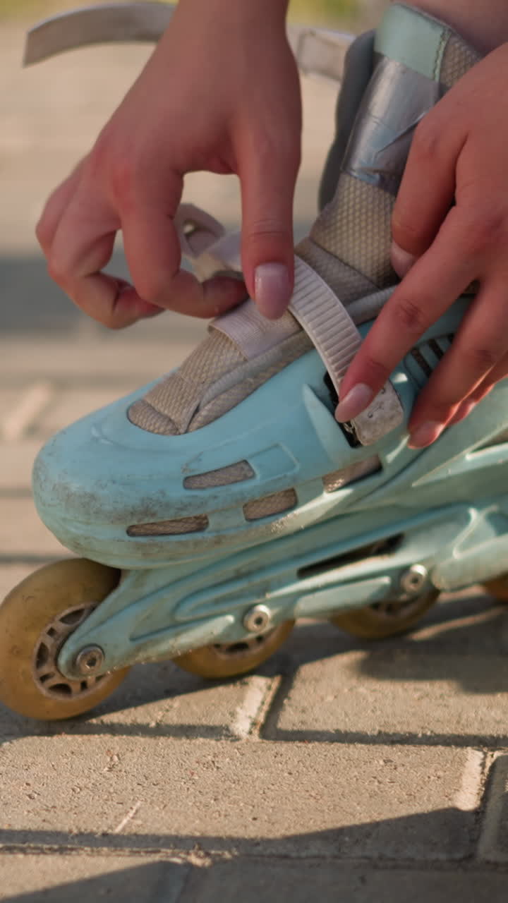 Close-up of individual adjusting strap on left roller skate with careful attention to secure the buckle, capturing detailed hand positioning, white sneakers visible in background