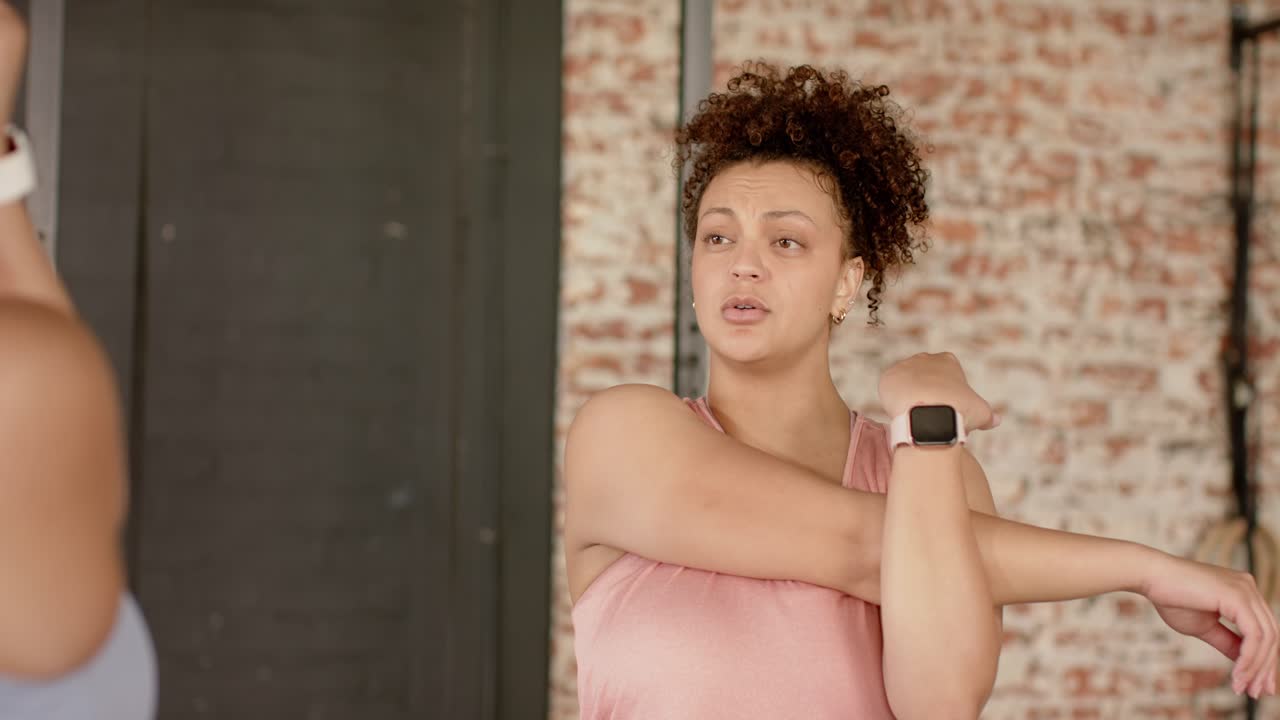 Istruttore che dà istruzioni a una donna in canotta che stira il braccio sinistro sul petto in palestra per il riscaldamento.