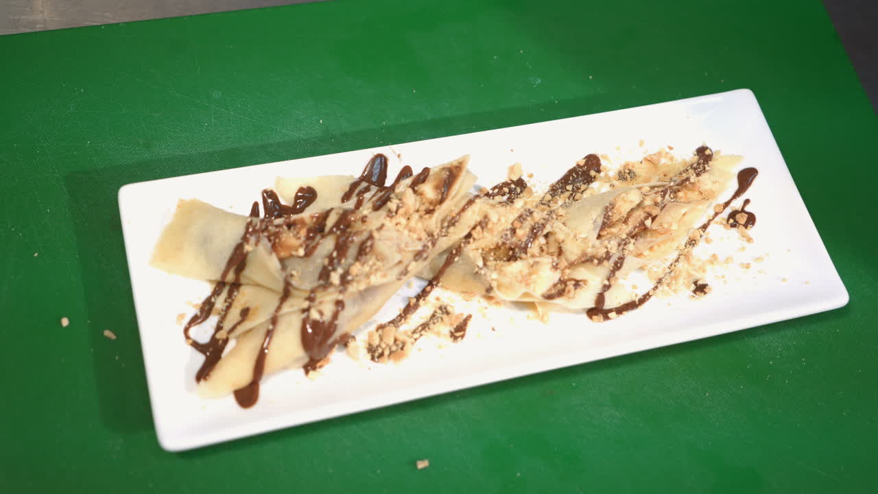 Chef is working on the presentation of the dish in a commercial kitchen. Pancakes with chocolate sauce on a plate