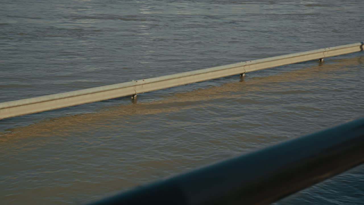 Submerged guardrail in flooded river, calm water surface reflecting light, Budapest, Hungary