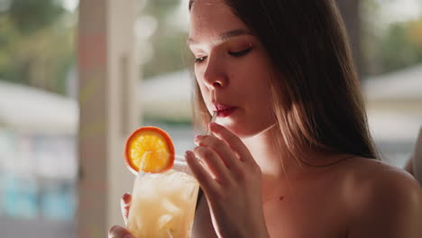 young lady drinks cocktail through straw in bar. sad woman enjoys fruity taste resting alone in beach bar. guest suffers from loneliness at party