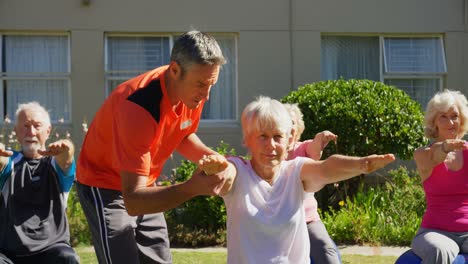 Vista-Frontal-De-Un-Entrenador-Masculino-Caucásico-Entrenando-A-Personas-Mayores-En-La-Realización-De-Yoga-En-El-Jardín-De-Enfermeras.