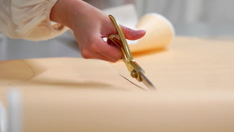 Young-female-designer-with-tape-line-on-her-neck-standing-in-dressmaking-studio-and-drawing-lines-with-chalk-and-rule.-Female-couturier-in-atelier-cutting-out-a-pattern-for-future-clothes.-handmade-tailoring-of-exclusive-wedding-dresses