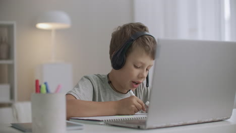 little boy is drawing sitting at table with laptop with green screen for chroma key technology child at home at weekend