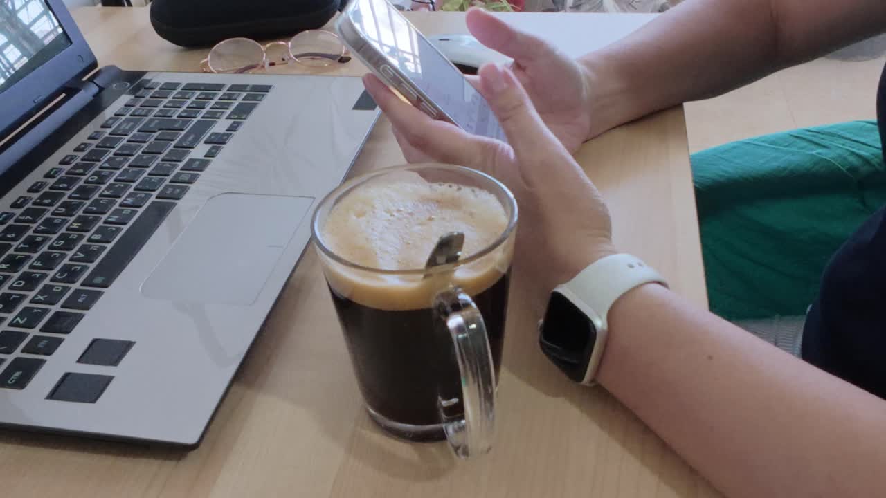 Freelancer's workspace: hands on phone, laptop, coffee. Essential tools for independent work