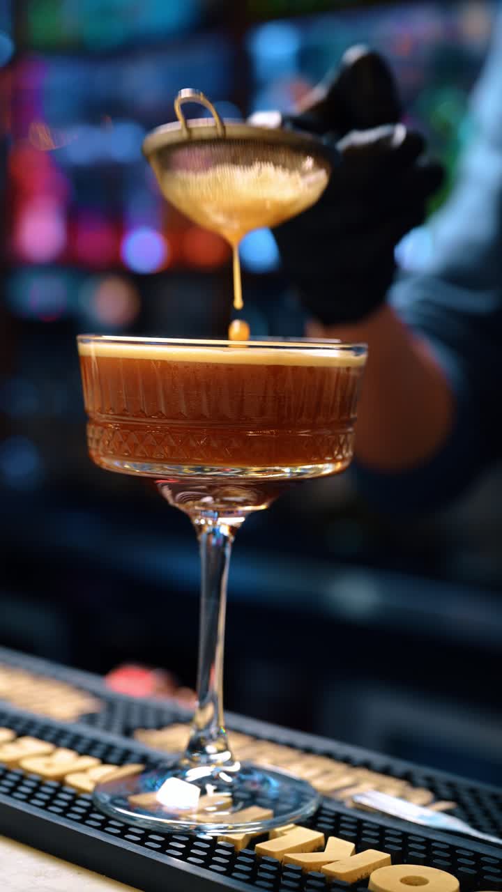 New York, USA, 15 aprile 2026: Barman che esegue una doppia filtrazione di un espresso martini scuro in un bicchiere a coppa. Primo piano del liquido che si versa attraverso un colino a maglie nel bicchiere su un tappetino da bancone del bar.