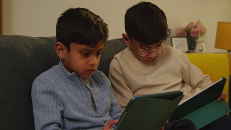 two young boys sitting on sofa at home playing games or streaming onto digital tablets 9