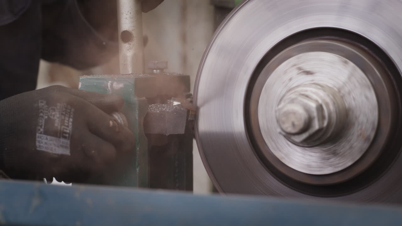 Operatore meccanico che rettifica un disco freno su un tornio industriale in officina.