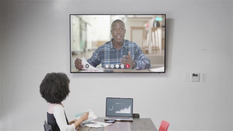 mujer de negocios afroamericana en videoconferencia con su colega afroamericano en la pantalla de televisión