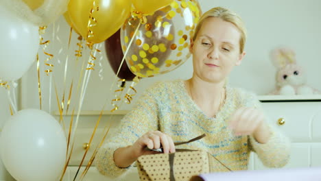 mom wraps a box with a gift in wrapping paper sits by the bed in the children's room decorated with