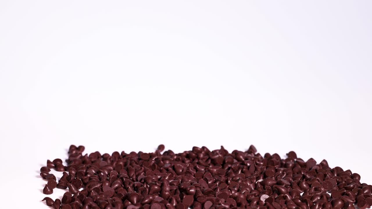 Chocolate pieces cascade onto a pile, set against a clean white background. The video captures the dynamic motion and rich texture
