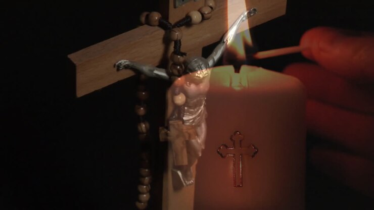 Animazione di croce con rosario su mano che accende una candela su sfondo nero