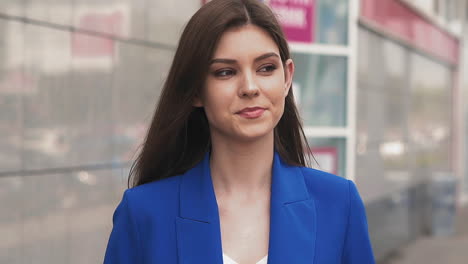 smiling woman in blue suit adjusts hair walking along street