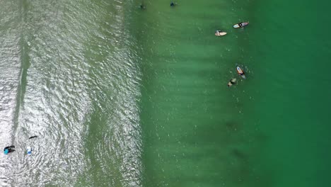 Bird-eye-aerial-over-beach-waters-and-people-on-surf-boards-gently-floating-on-sea-waves,-location-Lombok's-Selong-Belanak-Beach,-a-tropical-haven-on-the-Indonesian-island